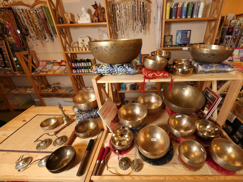 Ein Holztisch und ein Regal im Laden Traumstein, dicht an dicht mit Klangschalen aus Messing in verschiedenen Größen, dazu Klöppel, Fingerzimbeln und bunte Kissen.